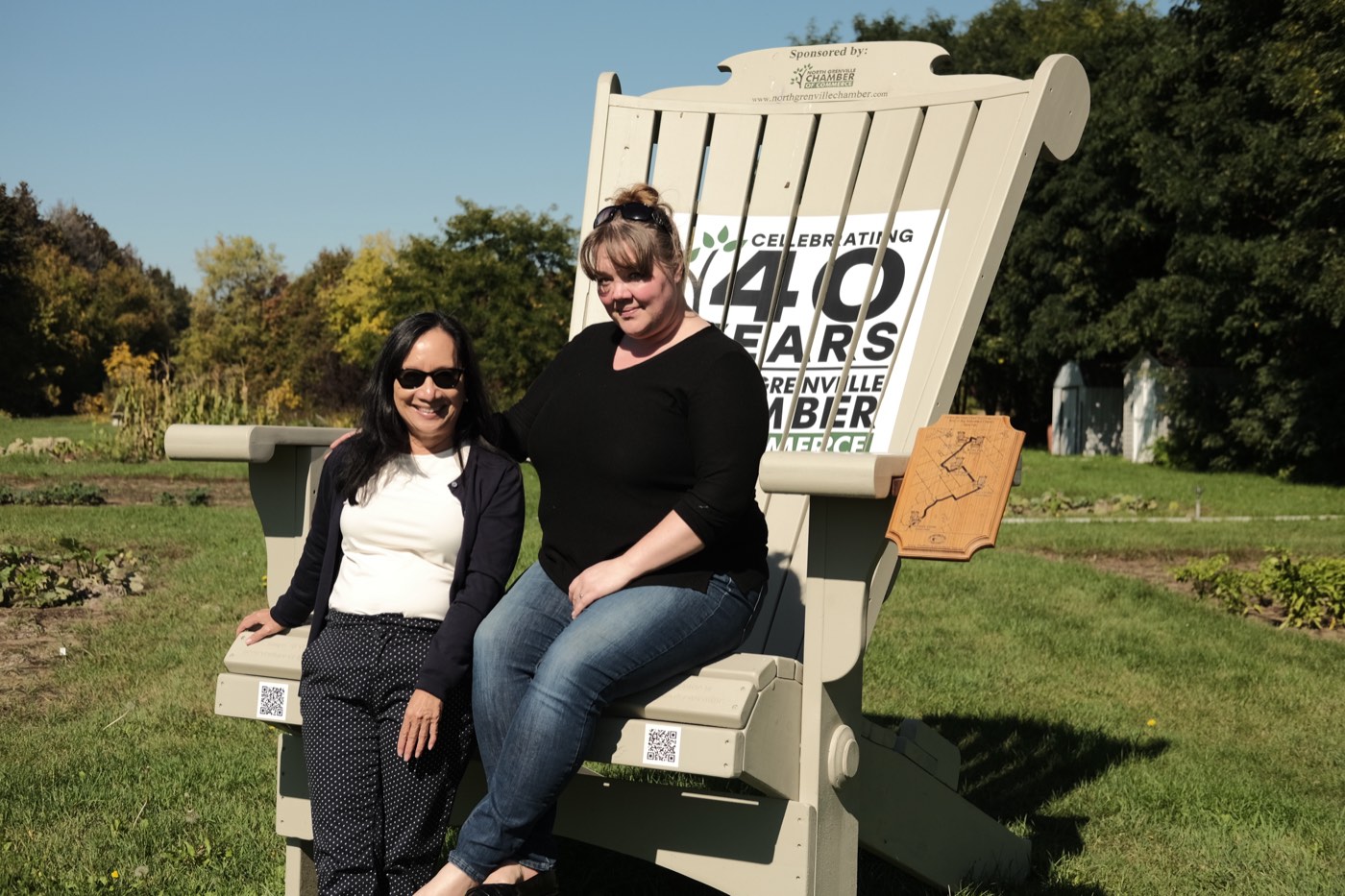 Two people sitting on an oversized Adirondack chair marking the North Grenville Chamber of Commerce's 40th anniversary